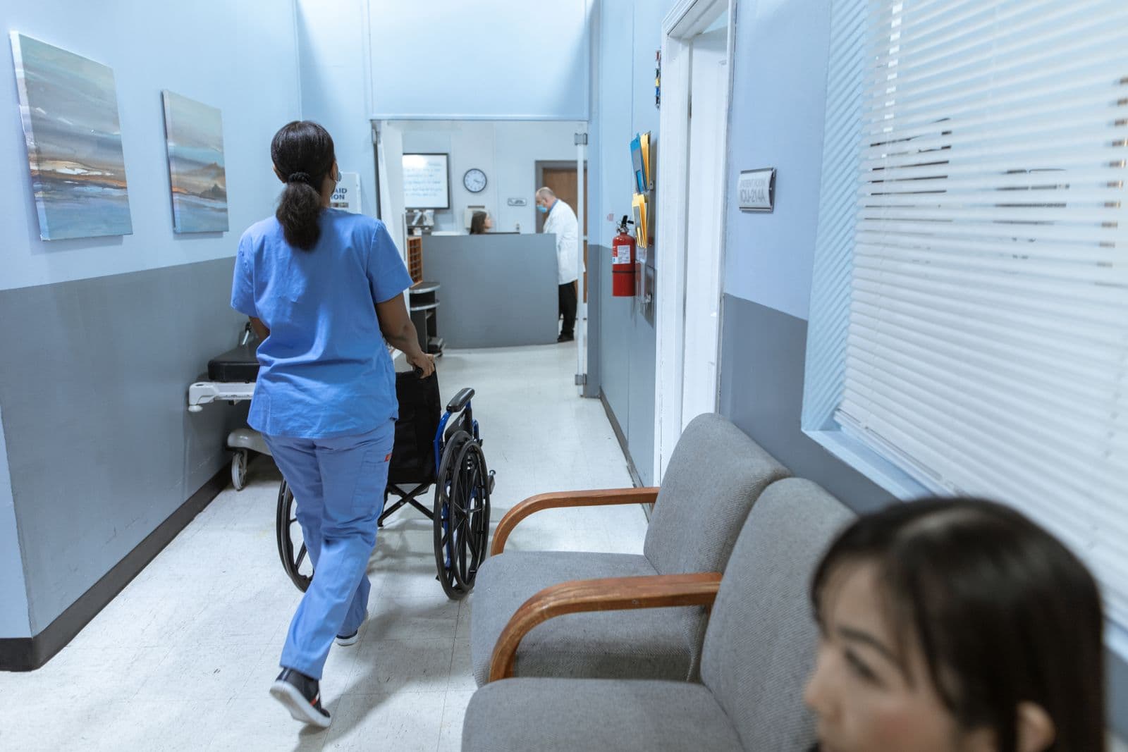 Fahrerin begleitet einen Fahrgast im Rollstuhl durch den Klinikflur